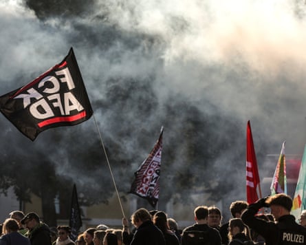 Police look on as demonstrators hold banners and flags, with one flag reading: ‘FCK AFD’.