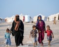 Displaced women and children walk across sandy ground near tents at a camp in Yemen