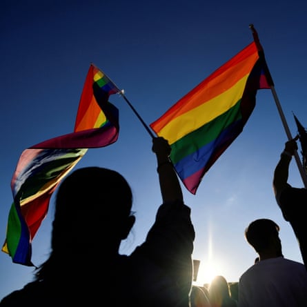 Silhouetted demonstrators wave rainbow flags
