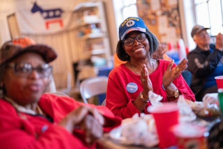Two smiling women in red shirts applaud at a table.