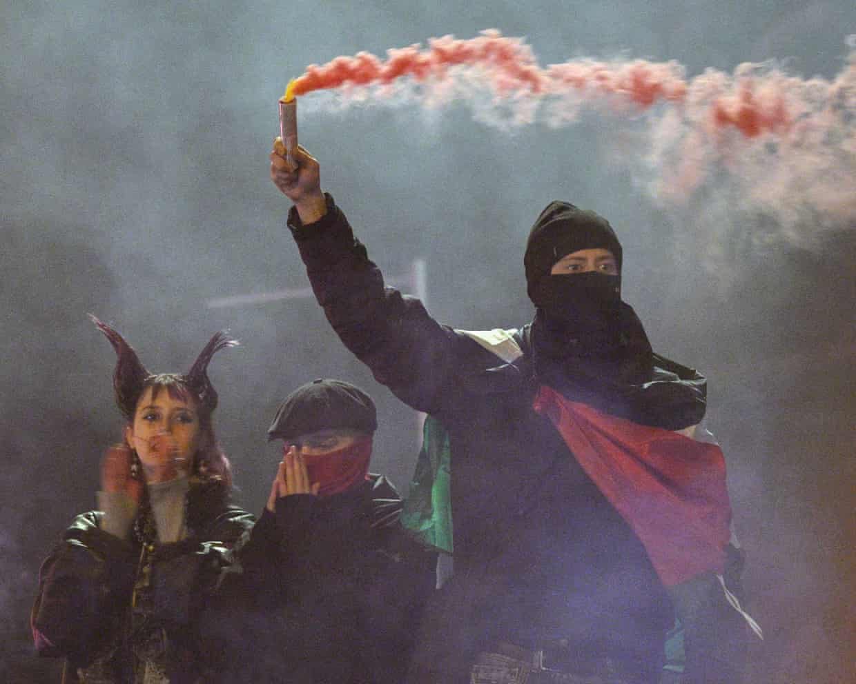 A masked protester raises a smoking red flare during a Berlin Gen Z demonstration