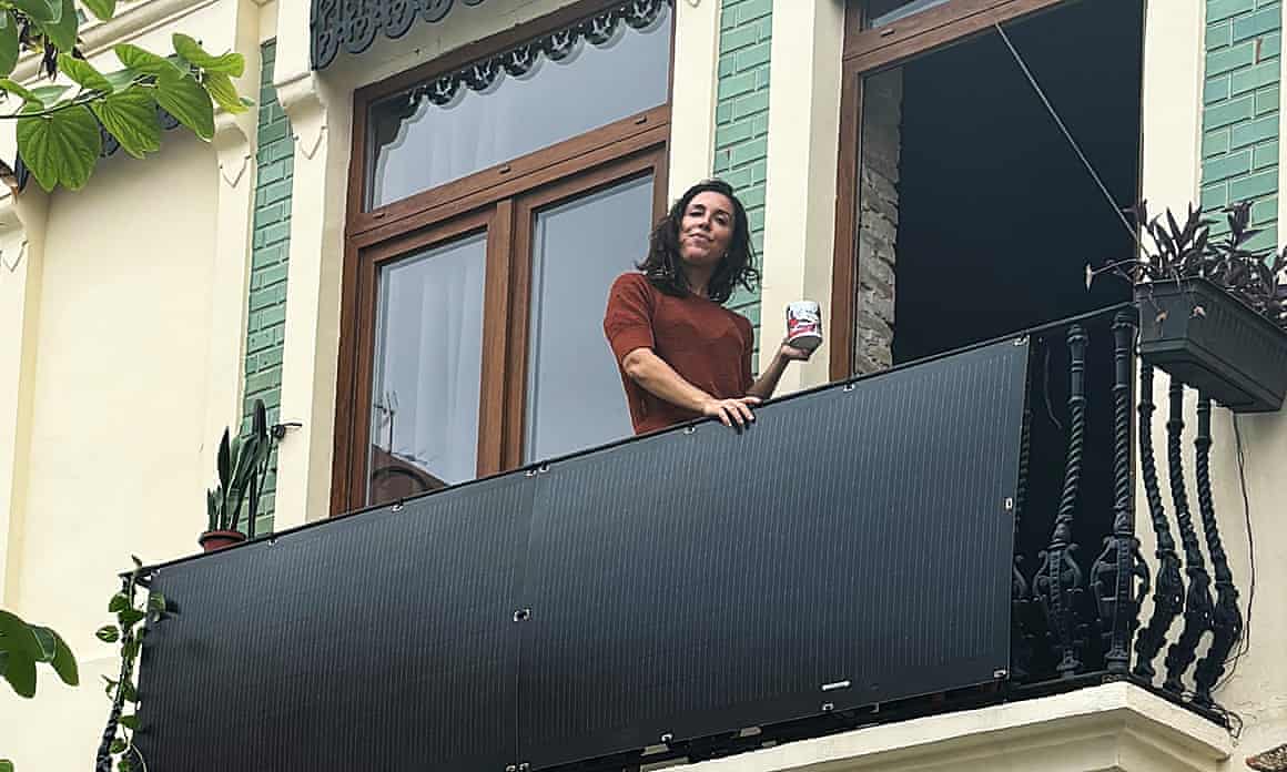 A woman stands on a balcony with a solar panel on the front of the railings