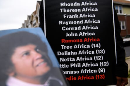 Mike Africa Jr holds up a sign listing the names of victims in the 1985 Move police bombing, with survivors highlighted in red.