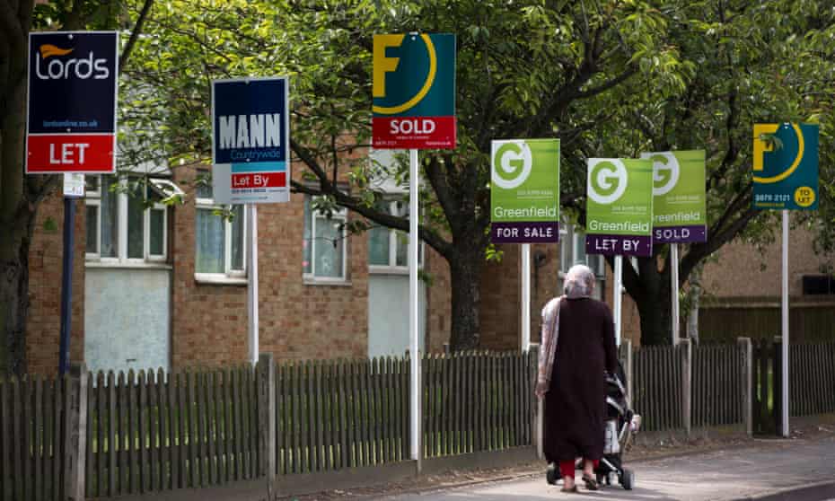 A pedestrian pushes a baby stroller as she walks past estate agent signs in the Kingston area of London