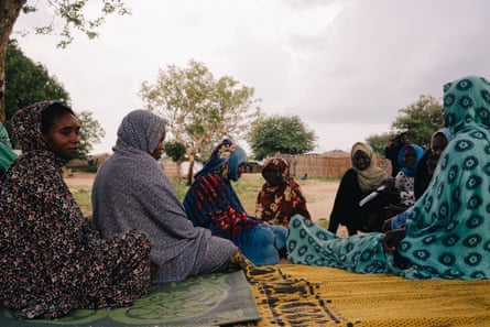 Sudanese women sit on mats under a tree