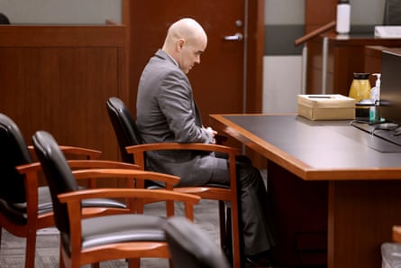 man wearing gray suit sits at table and looks down