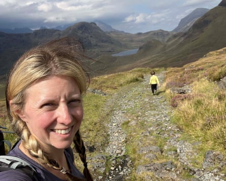 Woman taking smiley selfie with child on path and mountains behind