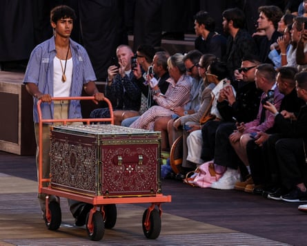 A model wheels a large ornate trunk down the catwalk