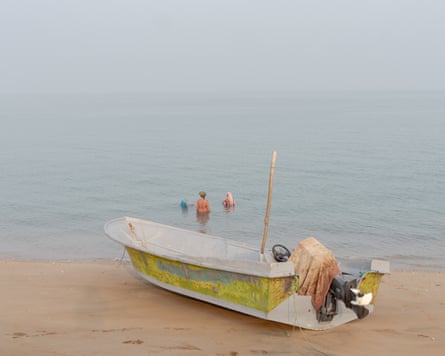 Boat on sand shore in foreground with people beyond in sea