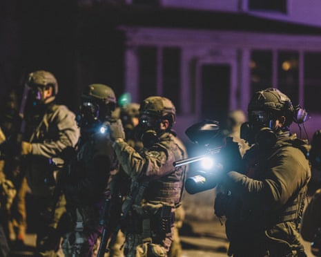 A line of men holding weapons wearing military style uniforms and with helmets and masks