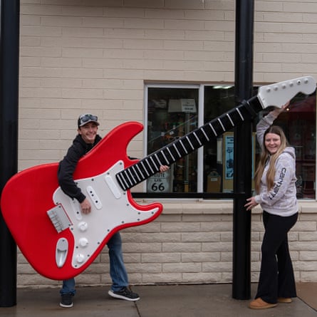 A couple standing outside a shop; the man is holding a model guitar twice his size