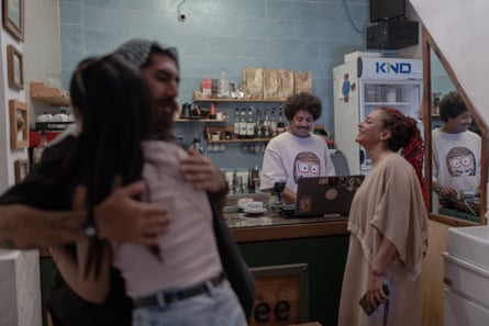 Two people hug in foreground with another two behind chatting at till