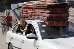 A child looks out of the window out a white car that has thin mattresses strapped to the roof