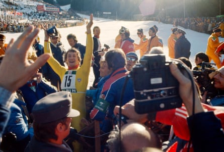 Klammer at the bottom of a ski run holding his arms up triumphantly, surrounded by crowds of people.