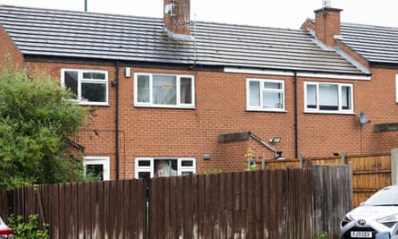 The rear of several square, brick terraced houses, with white window frames, tiled roofs and a high wooden fence around the back gardens
