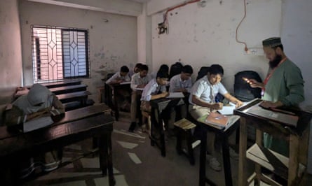 Seven schoolboys and a girl in a dark classroom, with a teacher holding his phone with the light on at the front of the class