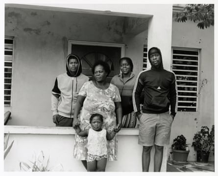 Five people and one small child stand outside a house with slatted windows