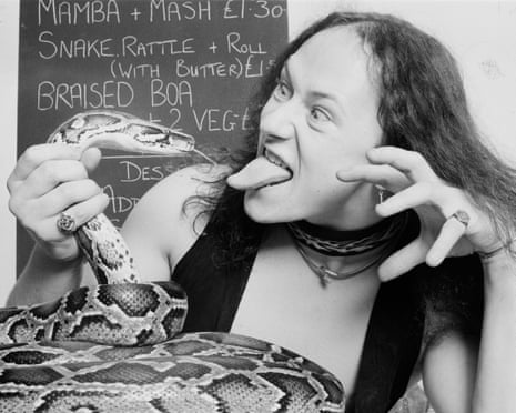A black and white photo of Venom frontman Cronos holding a snake by the throat as they both stick their tongues out at one another