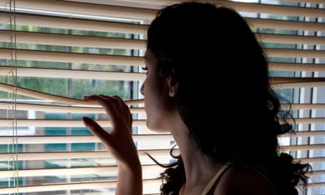 Young woman looking out of a window blind in a dark roomBETWN2 Young woman looking out of a window blind in a dark room