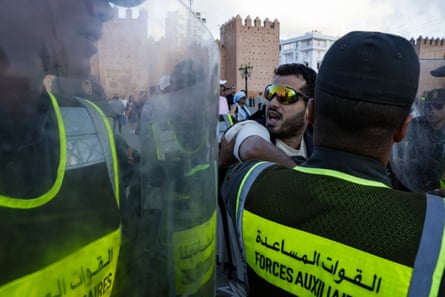 Police in riot gear up close to a protester wearing sunglasses.