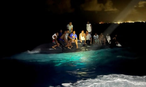 Survivors of a migrant boat that capsized perch on the overturned vessel off the coast of New Providence island, Bahamas, on Sunday.