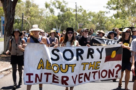 Manifestantes marchando sosteniendo una pancarta que dice '¿Perdón por la intervención?'