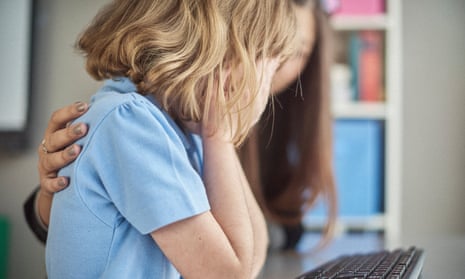 A worried schoolchild at a computer in a school and crying into her hands while a teacher puts an arm around her for support (posed by models)