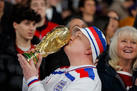 An England fan in a retro shirt kisses a pretend World Cup trophy