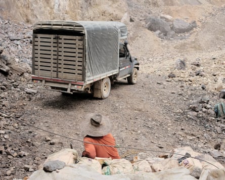 A truck drives up a dirt mine track away from a person wearing a wide-brimmed hat.