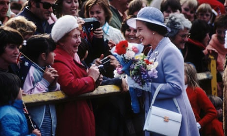 The Queen,  holding a bunch of flowers, talks to members of the crowd at a railing