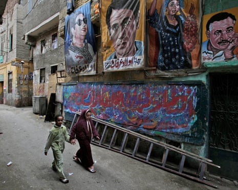 Two Egyptian girls hold hands as they walk past banners from left to right, depicting former Arab singing star Umm Kolthoum, former Egyptian singer Abdel Halim Hafez, and former Egyptian president Gamal Abdel Nasser, with Arabic writing that reads, “Arafa’s children,” in Cairo, Egypt, Wednesday, Feb. 1, 2012. (AP Photo/Muhammed Muheisen)