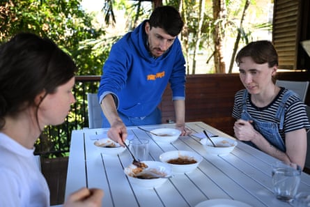 A man serves baked beans to his two friends sitting at a white table.