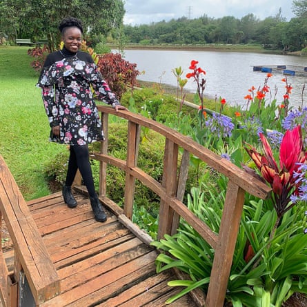 A smiling young woman poses on a wooden bridge beside a lake