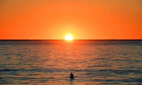 A surfer waits for waves during sunrise at Manly Beach in Sydney
