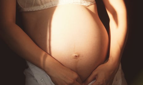 A light-skinned pregnant belly, identified elsewhere as Asian, with sunlight and shadows on it, encircled by the woman's arms.