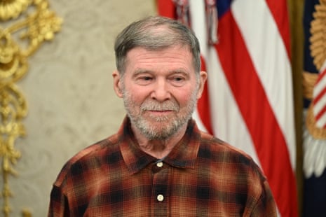 Stephen Hubbard, a bearded man in a plaid shirt, stands near a US flag