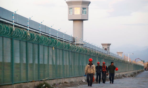 Workers walk by the fence of a detention centre for Uighurs in Xinjiang, China