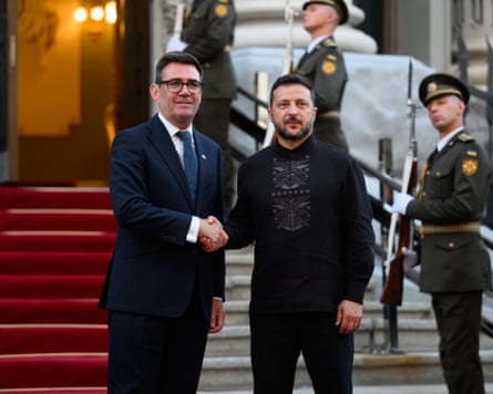 Burnham and Zelenskyy shaking hands in front of an ornate building with a red carpet running up the stairs and soldiers in ceremonial uniforms standing guard