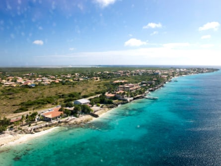 Aerial view of Bonaire showing a deep blue sea and small houses along the coastline. The land meeting the beach is very flat.