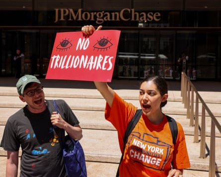 Two protesters, 1 holding a motion reference 'No trillionaires'.