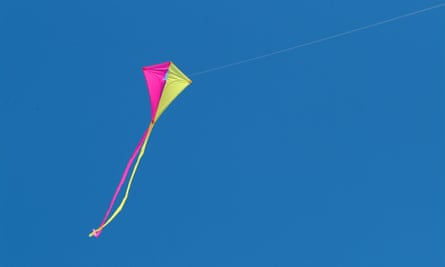 A pink and yellow kite flies against a blue sky, with two long ribbons tailing off it. 
