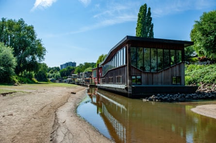 Pontoon-style houseboats rest on the muddy bottom of a dried-up river with just a narrow channel of water in the centre.