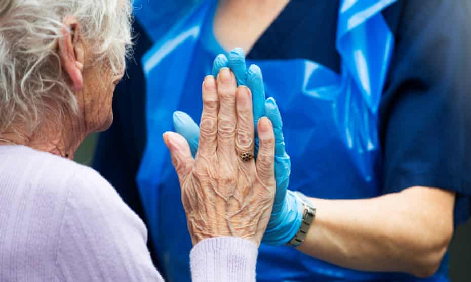 A care worker in gloves makes hand contact with elderly woman