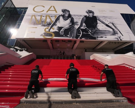 Workers roll a red carpet down a stairway