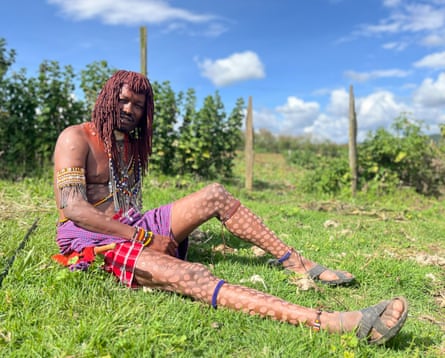 A Maasai man wearing a traditional plaid wrap and beaded jewellery sits on the grass in the countryside