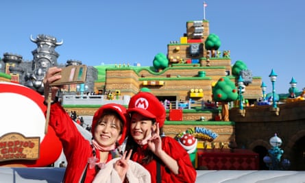 Two women wearing Nintendo merchandise take selfies in the theme park