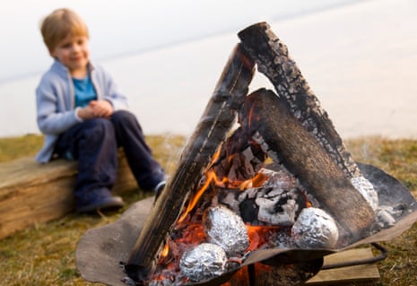 A boy looking at foil-covered potatoes baking in a campfire