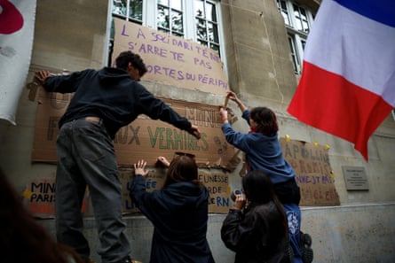 Students attach posters to the École nationale supérieure des mines in Paris where a French flag waves