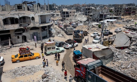 People standing in a street filled with cars and other vehicles amid the ruins of bombed-out buildings