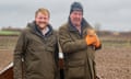 Jeremy Clarkson (R) holds a baby pig standing next to Kaleb Cooper in a cropless field